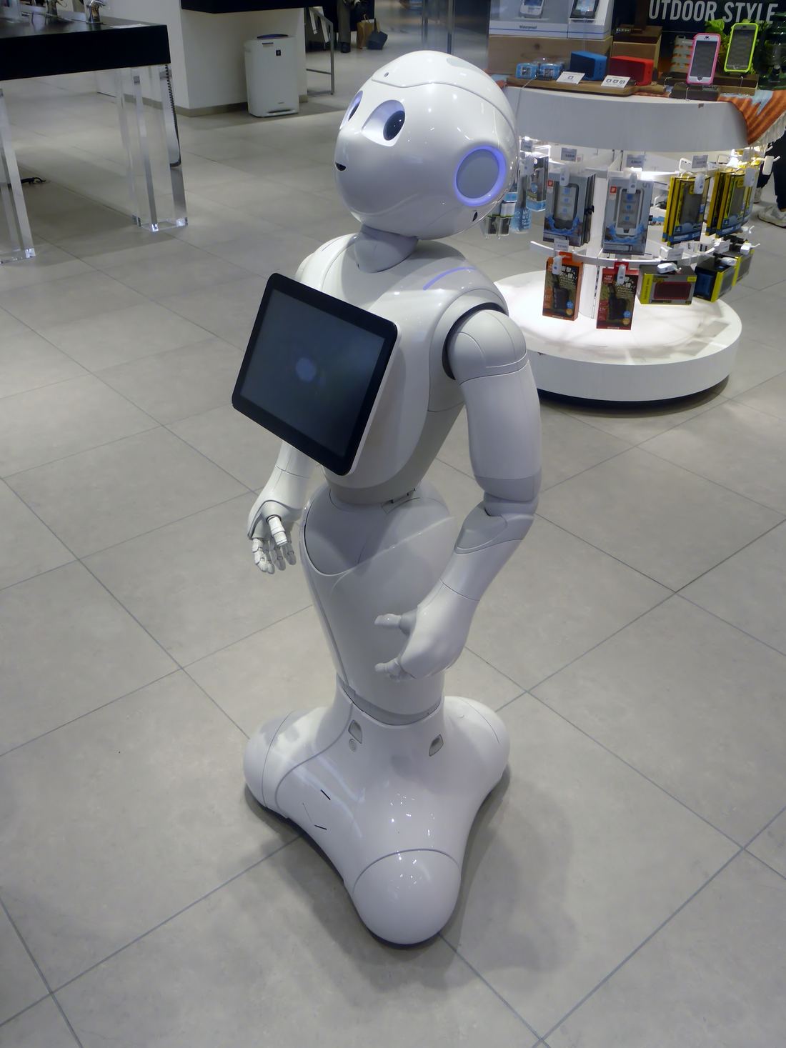 A white wheeled humanoid robot with a tablet on its chest in a shop