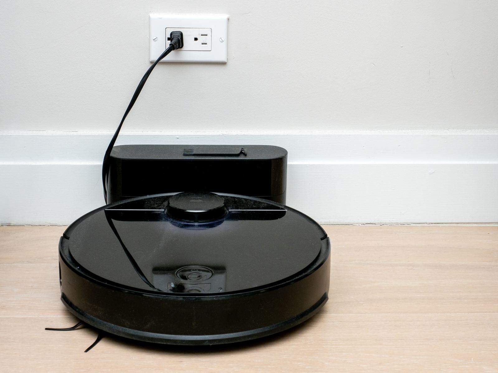 A round robot vacuum docked on its charging base on a wooden floor